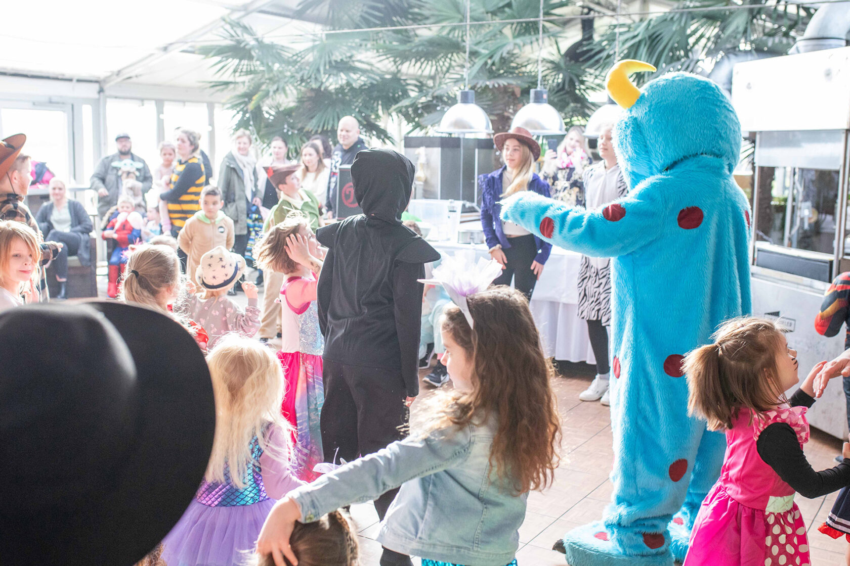 Kinder tanzen mit einem Maskottchen bei einem Familienfest auf den Hooksieler Skiterrassen